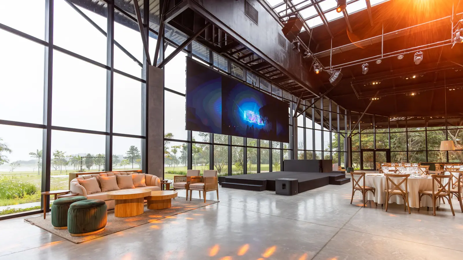 Event venue set with a large LED screen, a stage riser, an overhead lighting truss, lounge seating and banquet tables.
