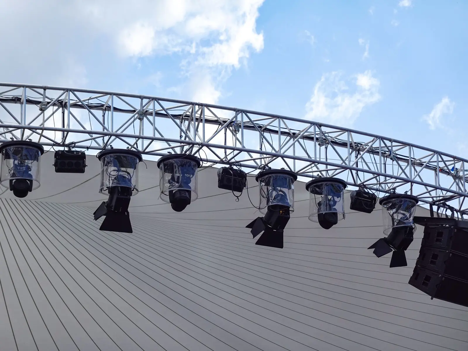 Lighting fixtures clamped to an overhead truss above a stage.