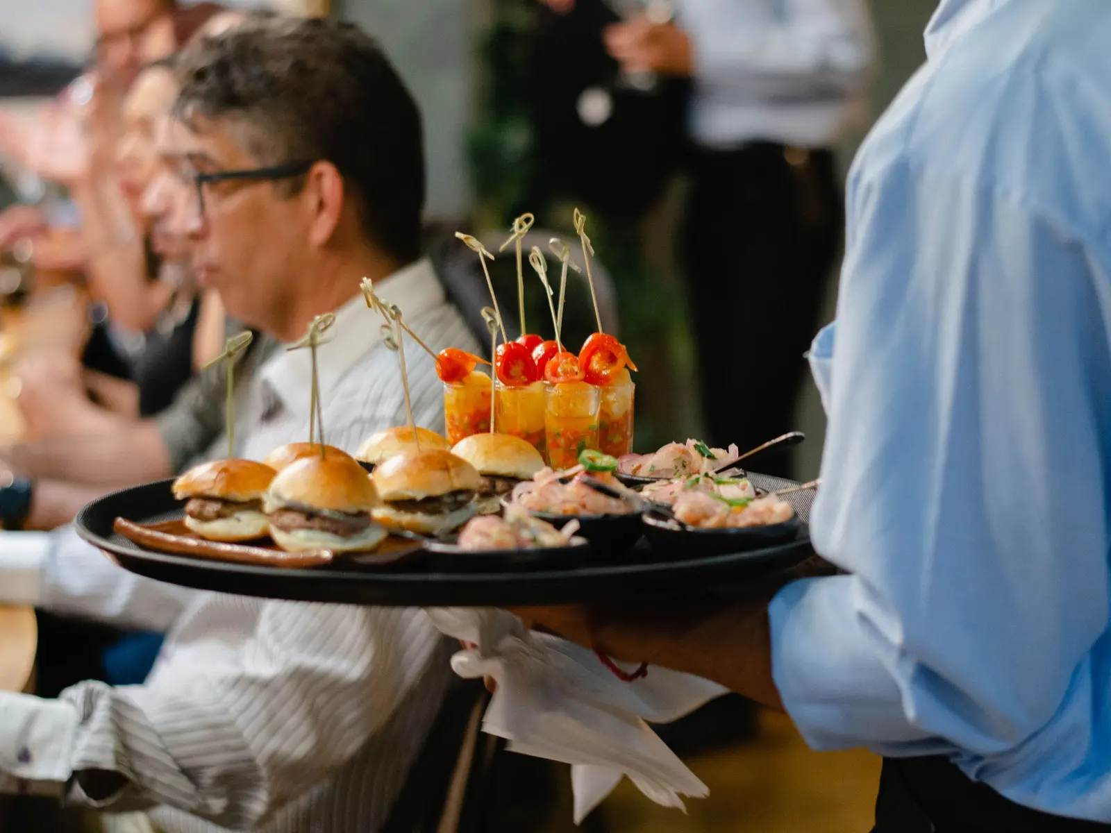 Waiter in uniform carrying a tray of canapes between guests.