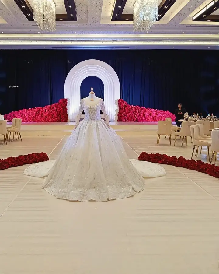 Bridal gown displayed on a white wedding runway framed by red flowers.